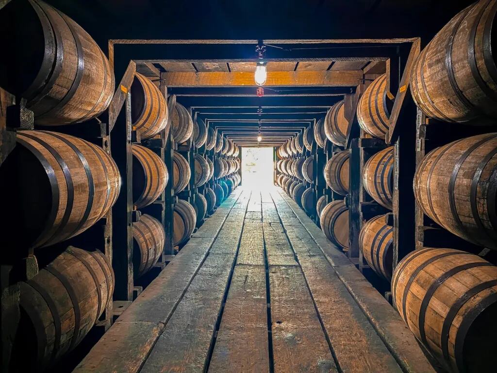 Rows of aging bourbon barrels lining a timber rickhouse aisle in Kentucky