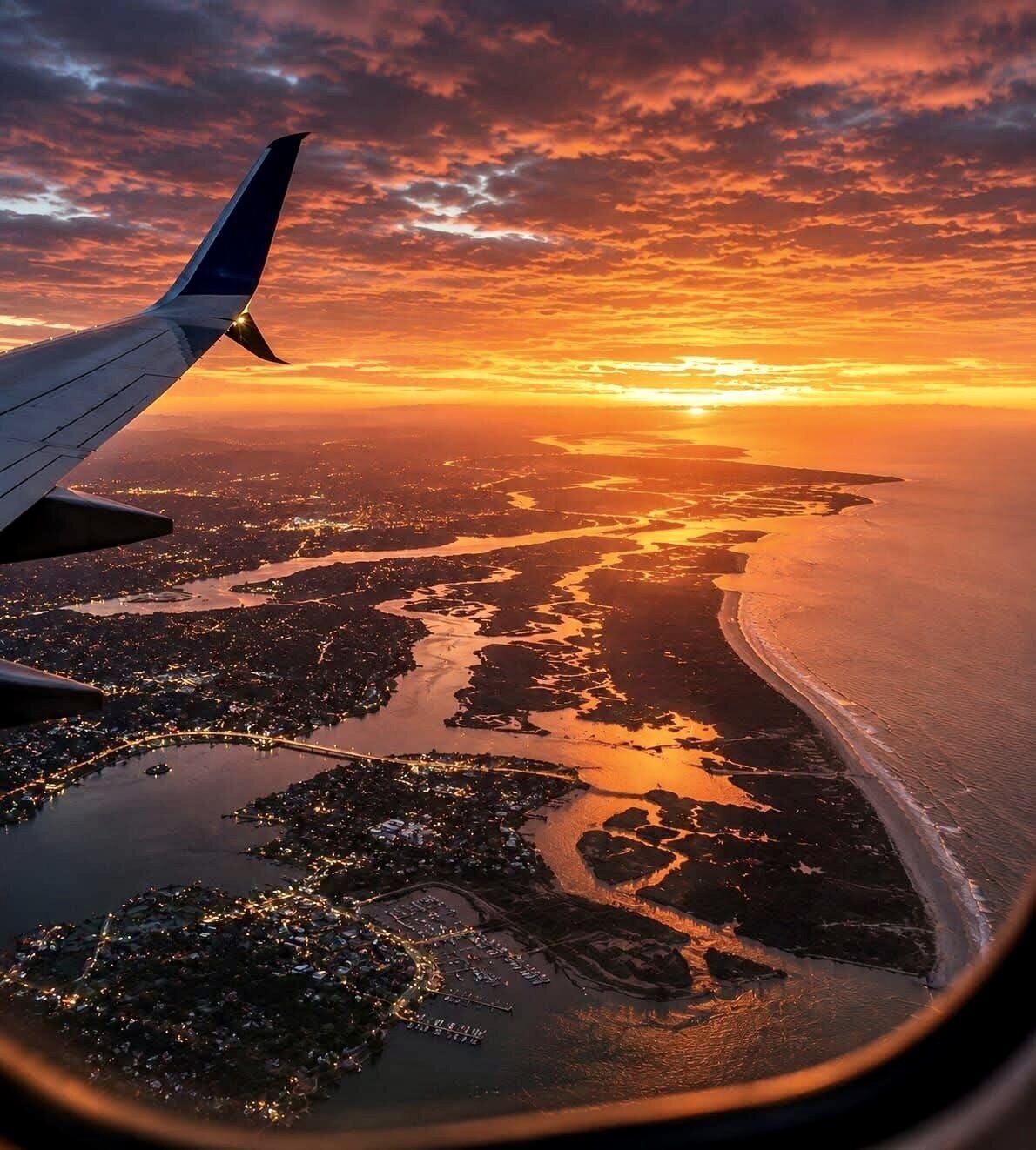 Airplane wing above coastal waterways and the Atlantic shoreline at sunset